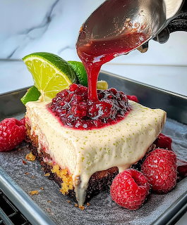 Slice of key lime cheesecake with graham cracker crust, topped with raspberry sauce and fresh berries