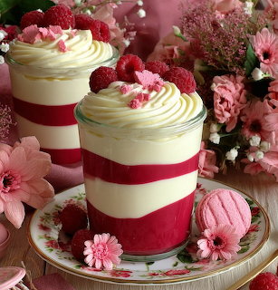 Layered raspberry and cream desserts in cups with fresh berries and pink flowers