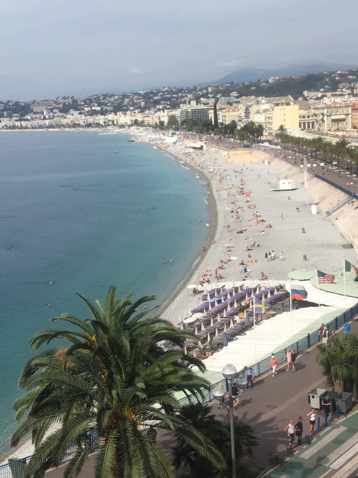 Coastal view of Nice beach and promenade with turquoise Mediterranean Sea, palm trees, and buildings along shoreline