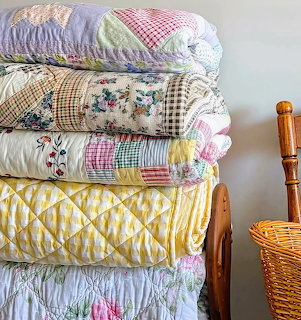 Stack of vintage patchwork quilts in pastel colors with floral and gingham patterns on wooden bed