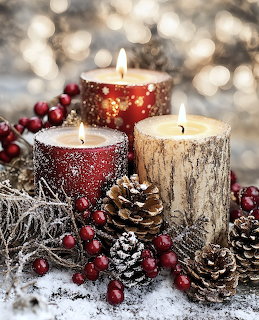 Three lit candles surrounded by pine cones, red berries, and white faux snow on a rustic winter holiday display
