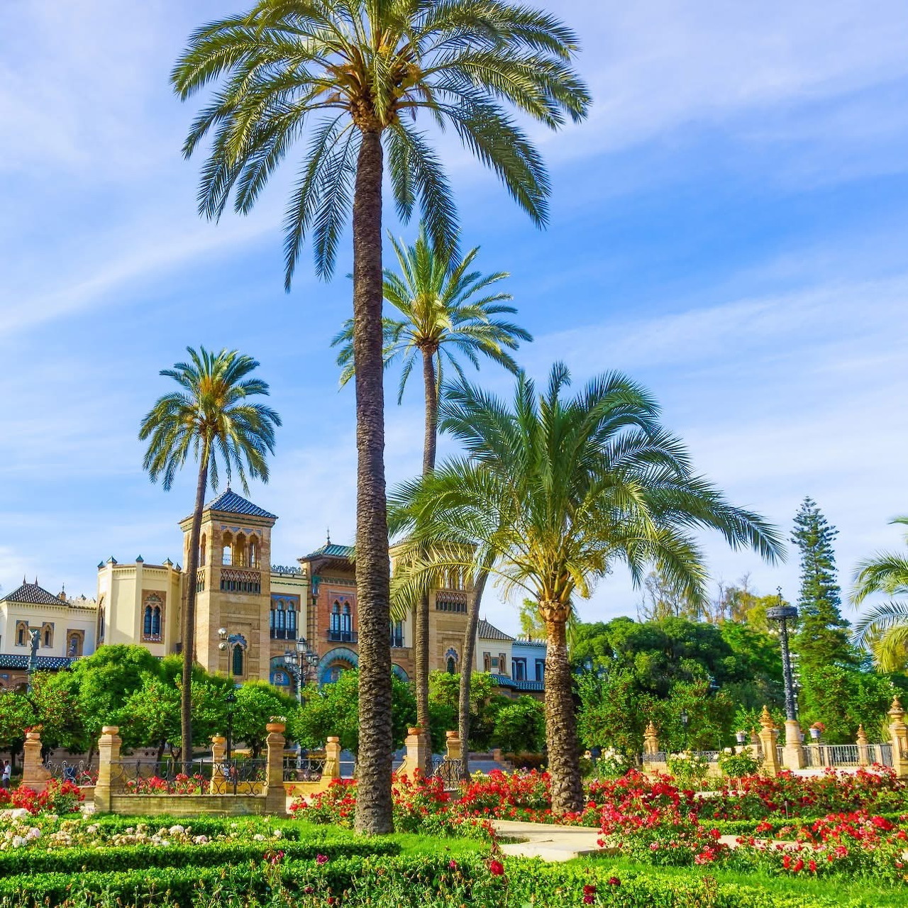 Palm trees and flower gardens in a Seville park with a historic building in the background