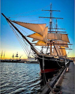 Tall sailing ship with orange sails docked at harbor during sunset