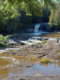 Rocky waterfall flowing through a forested river with exposed muddy banks in the foreground