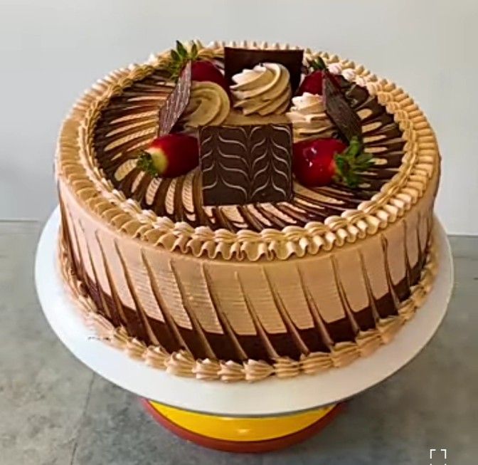 Round chocolate layer cake with decorative frosting, strawberries, and wafer stick sides on white pedestal stand