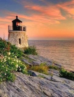 Stone lighthouse on a rocky shoreline at sunset beside the sea