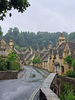 Wet road through a quaint stone village with old cottages and trees