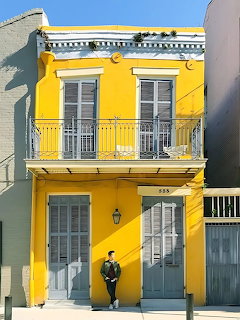 Bright yellow two-story house with white shutters and balconies, person standing at entrance