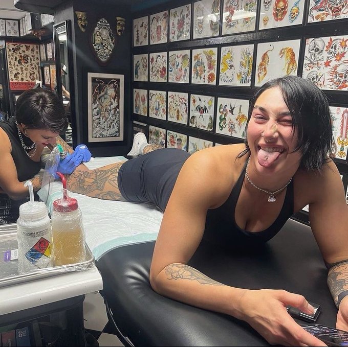 Smiling woman on a tattoo chair in a studio while a tattoo artist works on her leg