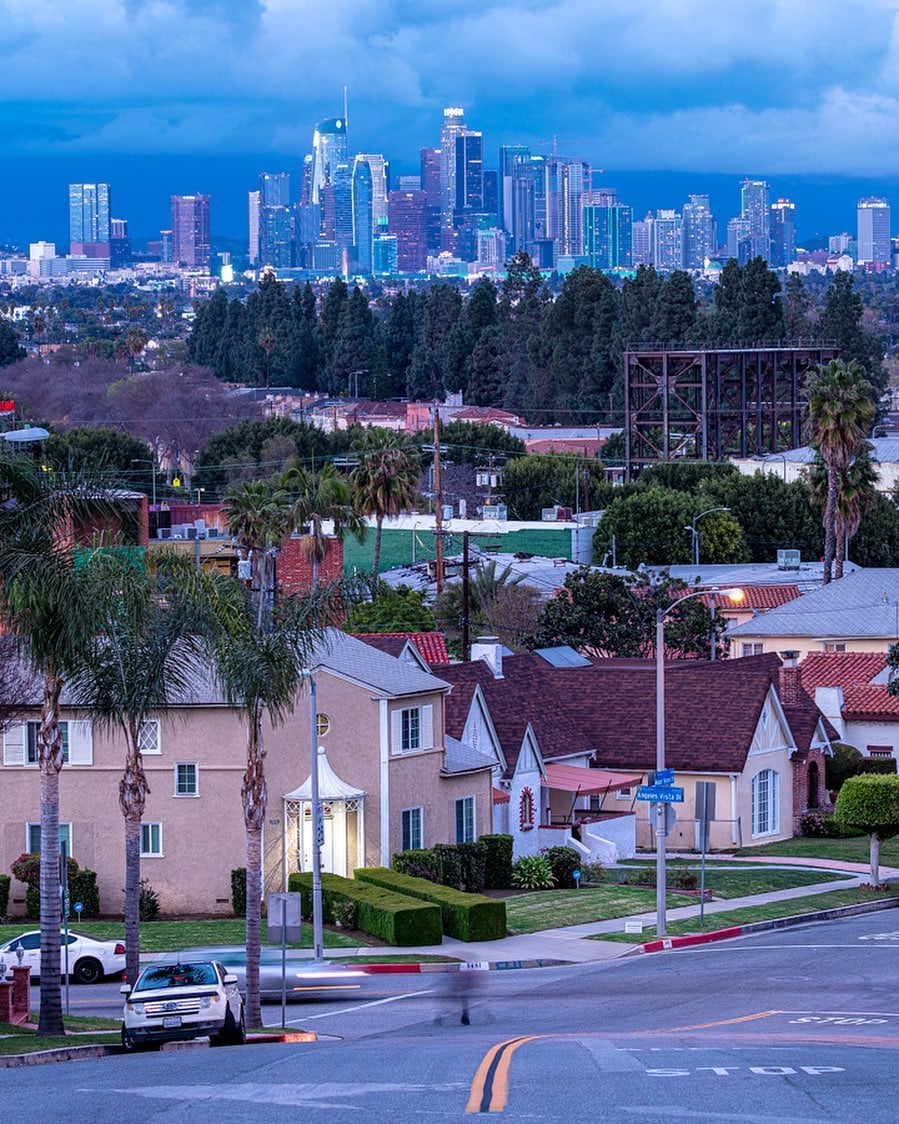 City skyline at dusk with residential area in foreground and downtown towers in background under blue evening sky