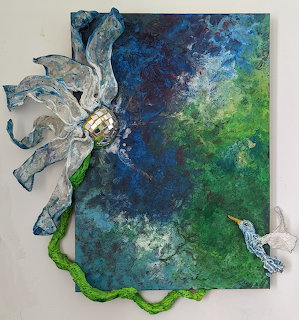Mixed media art with sculptural white flower and hummingbird on blue-green textured canvas