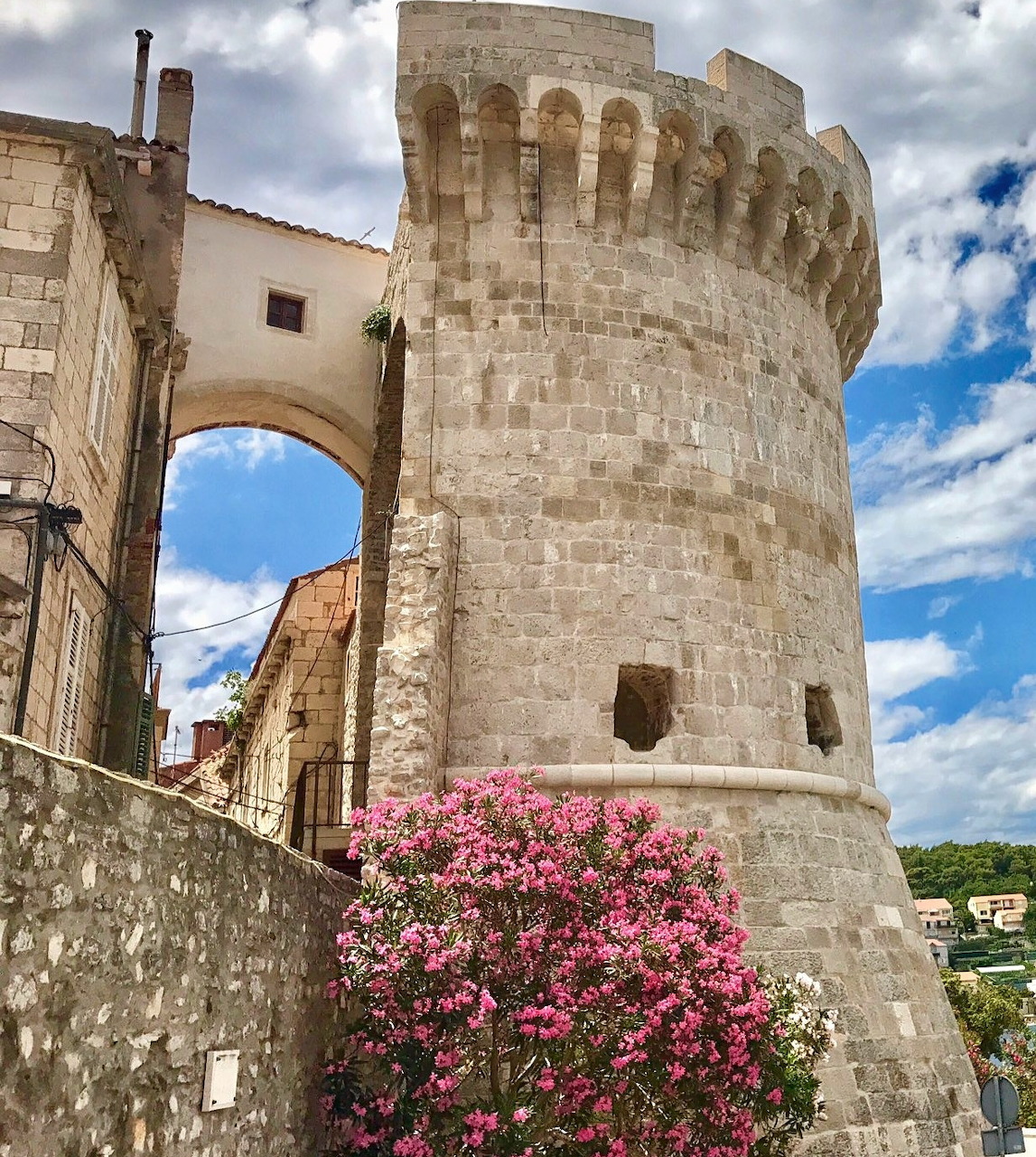 Medieval stone tower with pink flowers against blue sky in Korčula