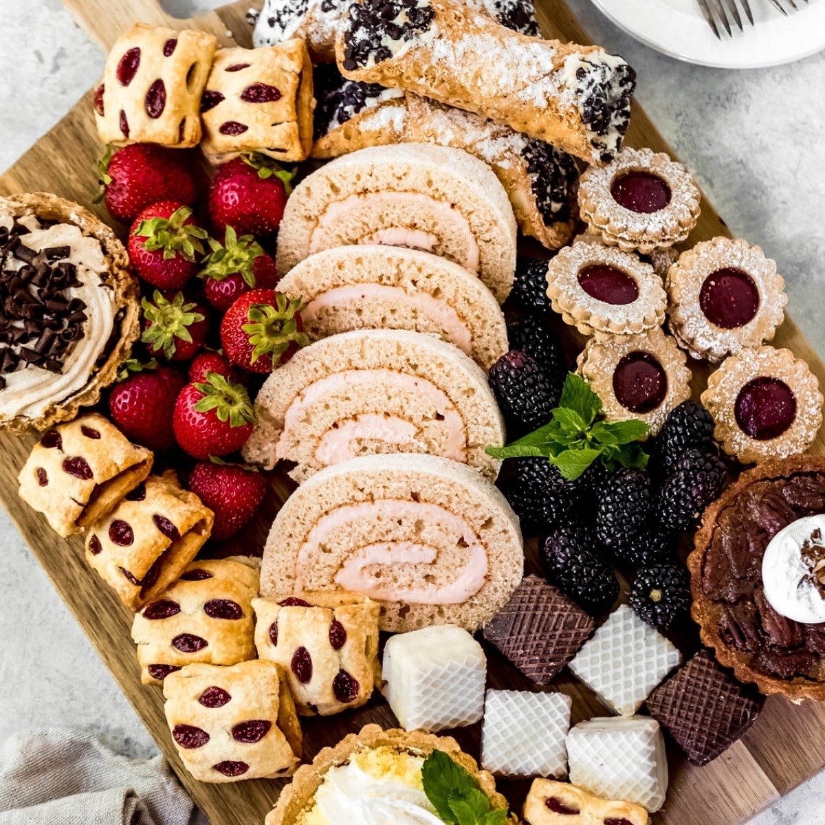 Overhead view of a dessert board with cookies, brownies, berries, and pastries on a wooden serving platter