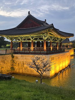 Illuminated traditional Korean pavilion with curved roof reflected in pond at twilight