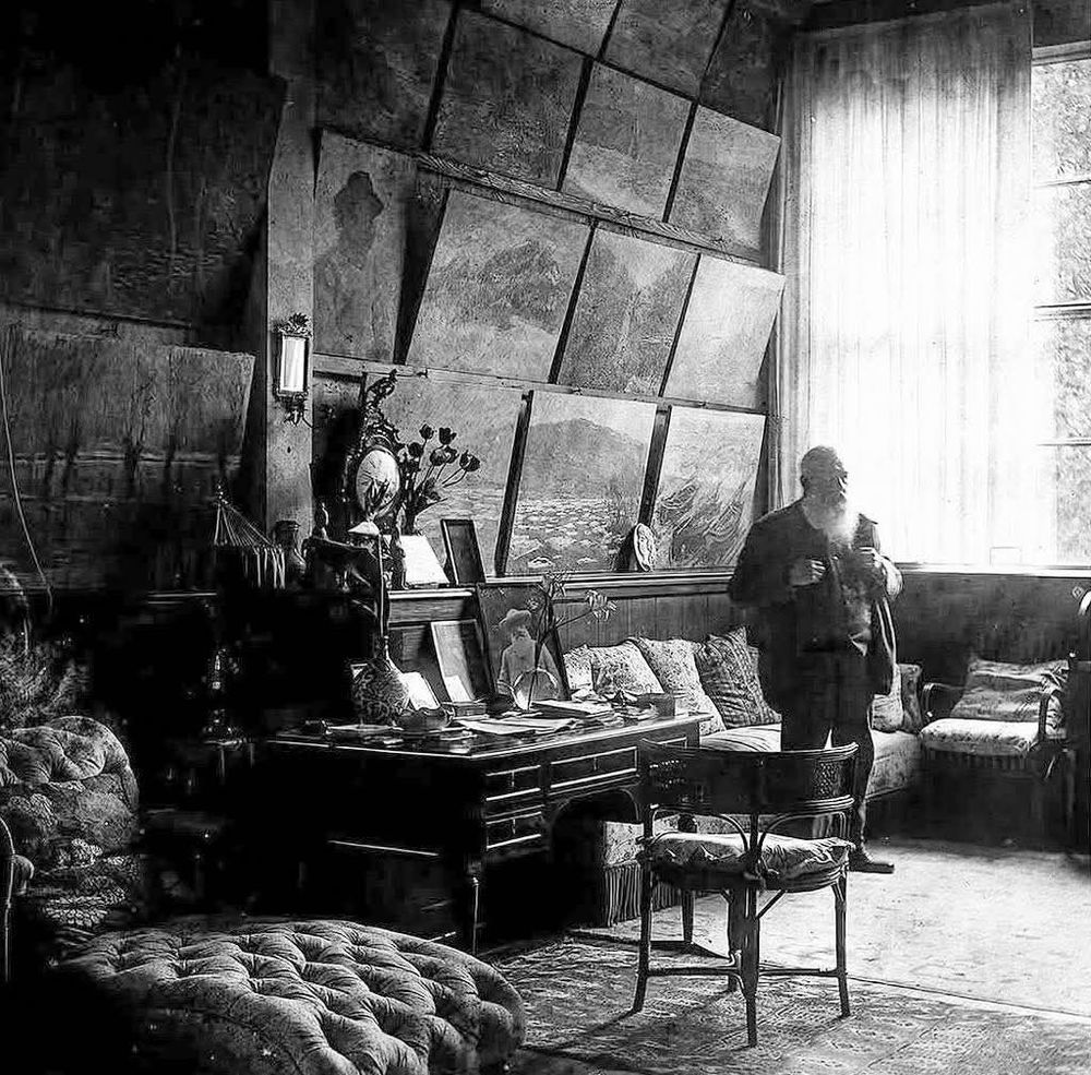 Black and white vintage room with canvases, chairs, furniture, and a person near a bright window
