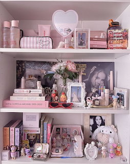 Pink coquette aesthetic shelf with books, perfume, flowers, figurines, and decorative items