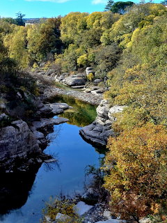 Rocky river gorge with calm blue water reflecting trees and sky, surrounded by autumn foliage and limestone rocks