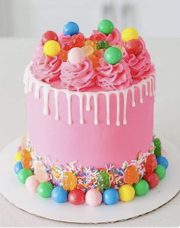 Pink frosted cake decorated with colorful candy balls, white chocolate drip, sprinkles, and pink buttercream swirls