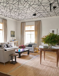 Modern living room with striking geometric black wire ceiling art, gray furniture, and natural light from tall windows