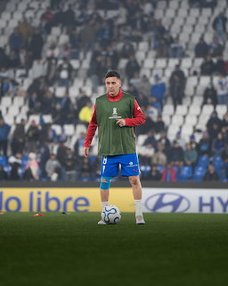 Soccer player in green training bib and blue shorts standing with ball on field during warmup