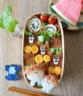 Kawaii-style bento box with cute food characters, sushi, rice, and watermelon on wooden surface