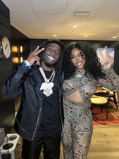 Two people posing together indoors making peace signs, one in black and one in a sheer patterned outfit
