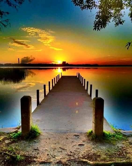 Wooden pier stretching across a calm lake at sunset with colorful sky reflections