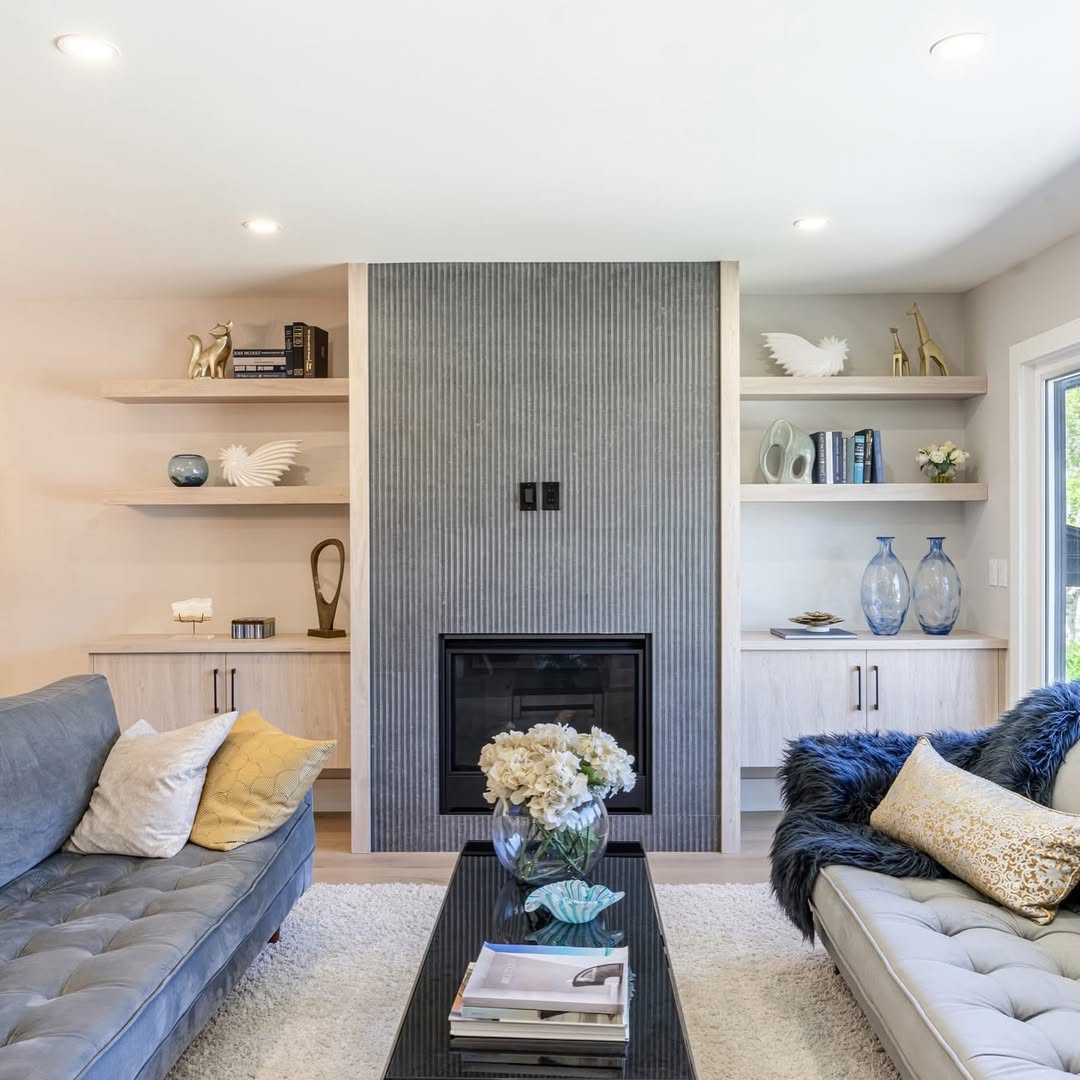 Modern living room with gray tiled fireplace, blue sofas, and white built-in shelves