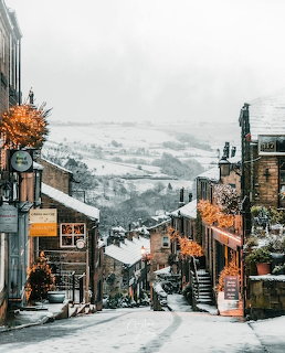 Snowy main street of Haworth village with stone buildings and hills behind