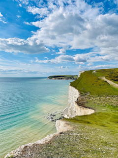 White chalk cliffs along turquoise ocean with green grass clifftops and blue sky