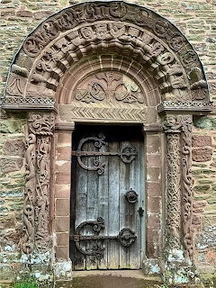Ornate Romanesque stone archway entrance with carved decorations and old wooden door at Kilpeck Church