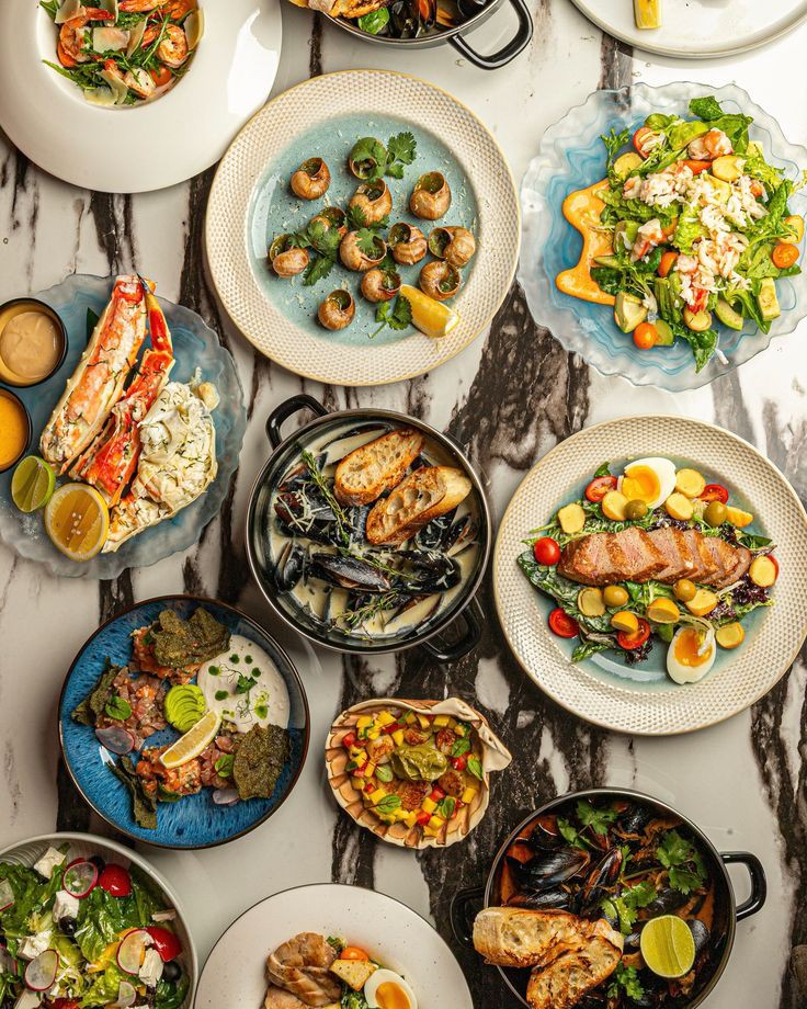 Overhead flat lay of multiple colorful gourmet meal dishes on marble surface