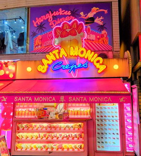 Neon-lit Santa Monica Crepes storefront at night with bright pink signs and illuminated menu displays
