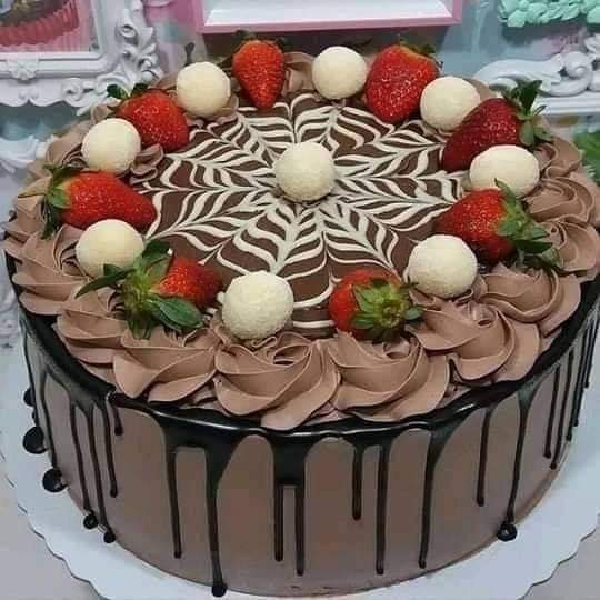 Chocolate drip cake topped with strawberries, white truffles, and swirled frosting