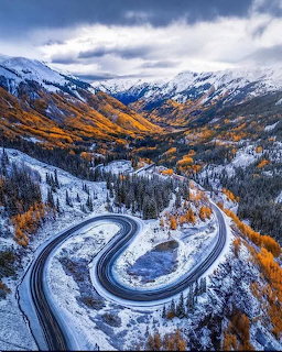 Winding mountain road with S-curves through snowy Colorado mountains with fall colors