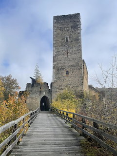 Medieval stone castle tower with wooden bridge leading to arched entrance, surrounded by bare trees and blue sky
