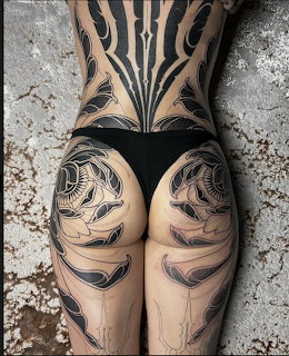Woman's tatooed back and legs with elaborate black ink tribal and organic designs, seen from behind