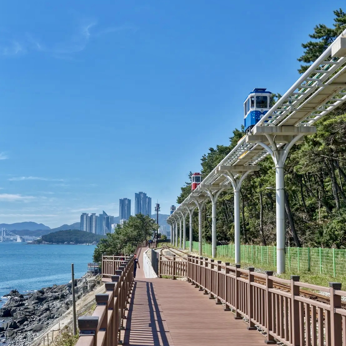 Cable car station above coastal boardwalk with ocean view and city buildings in distance