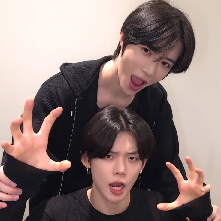 Two young men in black outfits making playful hand gestures and facial expressions
