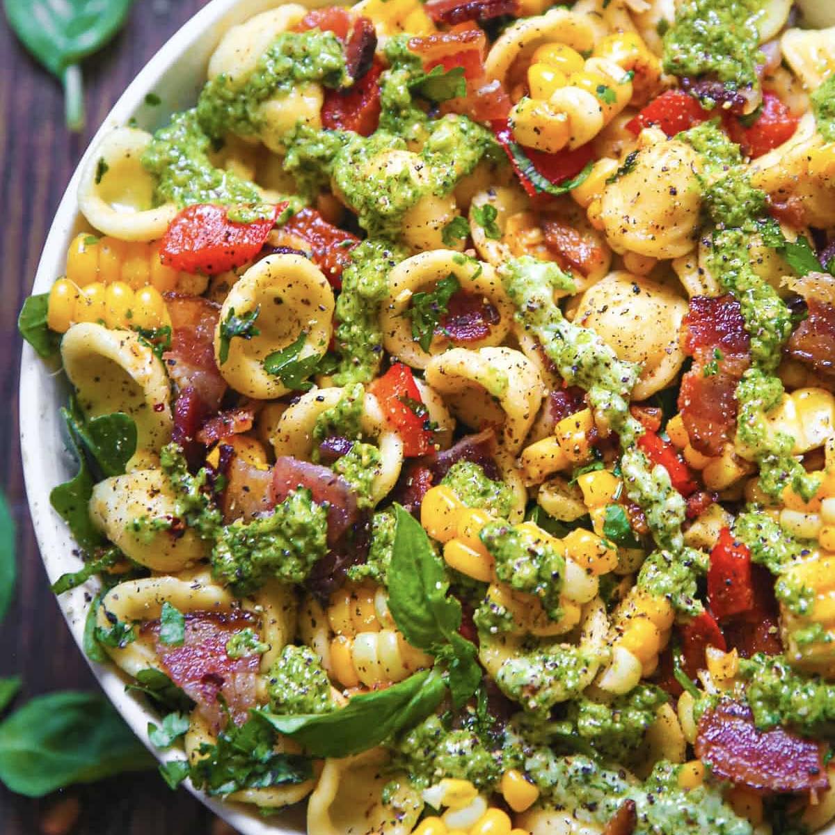 Bowl of pasta with corn, broccoli, bacon, and green pesto