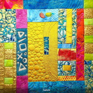 Colorful modern art quilt with geometric patchwork patterns in bright yellow, blue, pink, orange and green fabrics