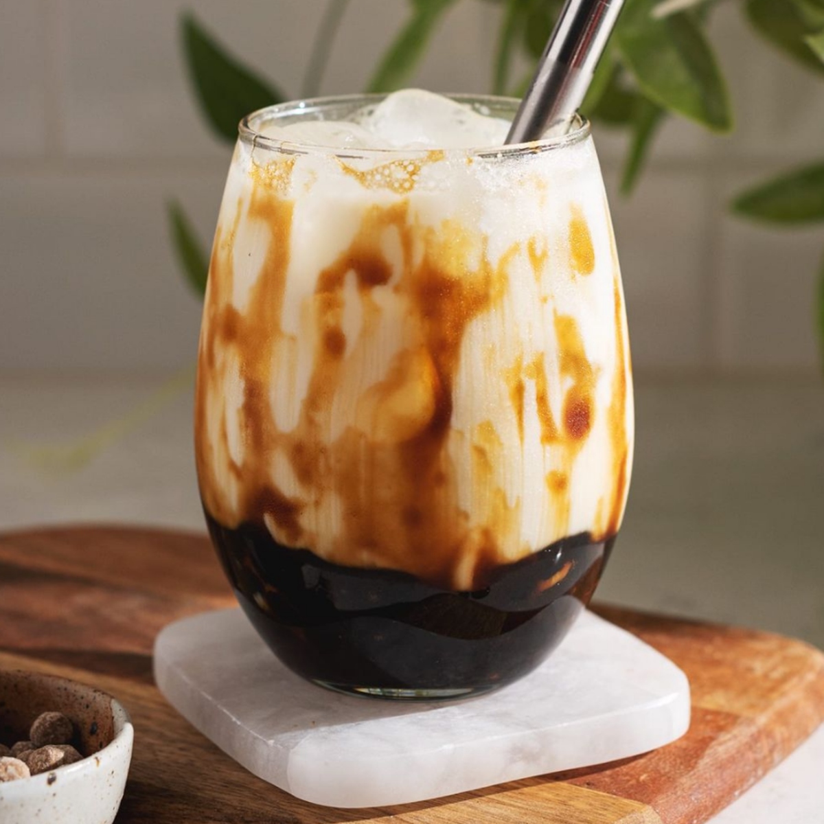 Glass of brown sugar boba milk tea with creamy swirls and tapioca pearls on a white coaster