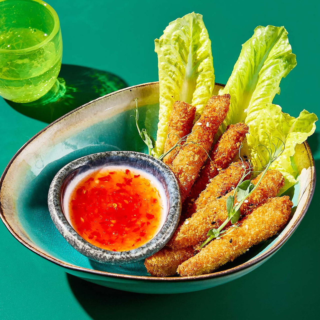 Crispy fried spring rolls with lettuce and sweet chili sauce in a teal ceramic bowl on green surface
