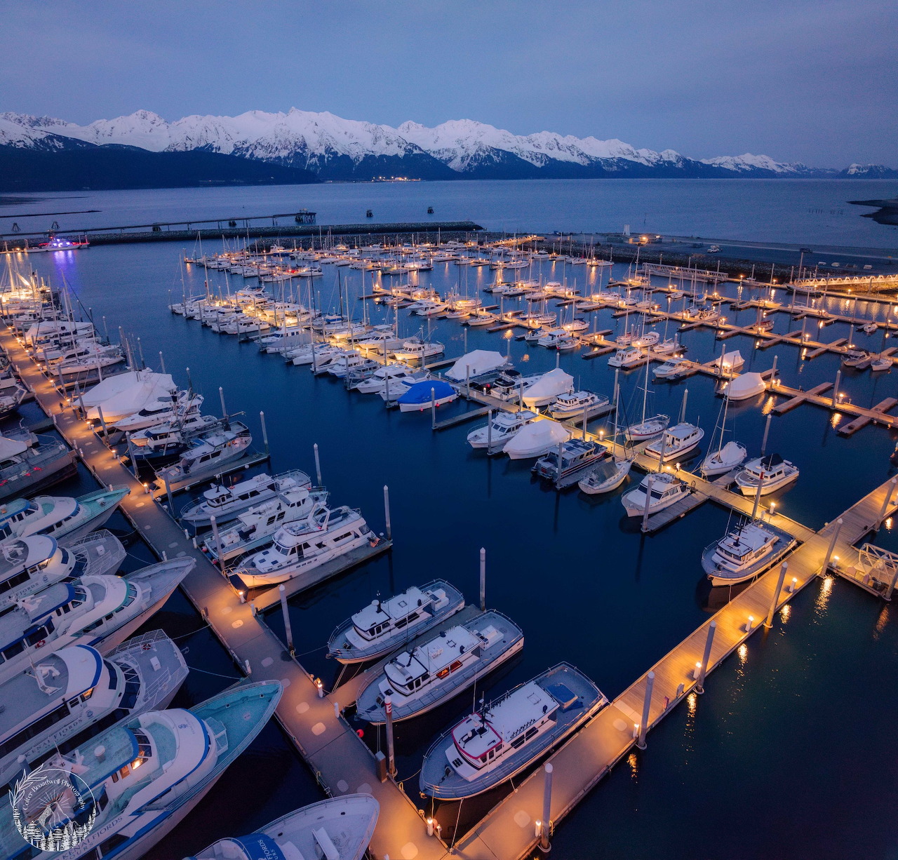Evening view of Seward Boat Harbor with docked boats, calm water, and snowy mountains beyond