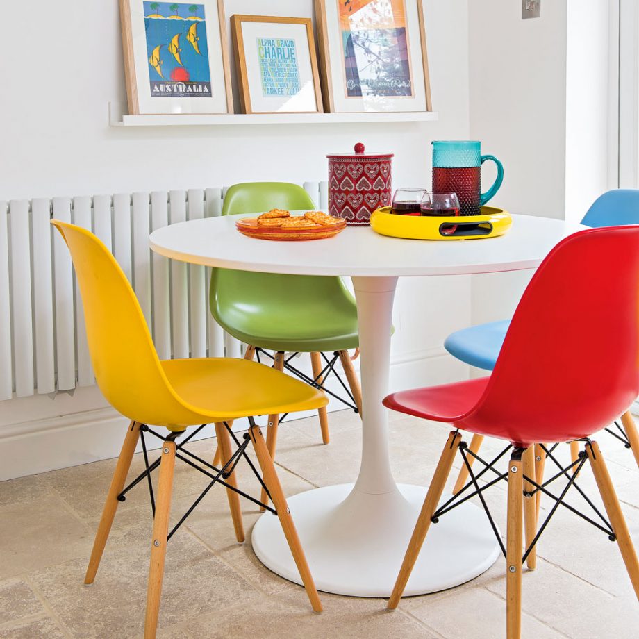 Small modern dining room with white round table and four multicolored chairs in yellow, green, and red
