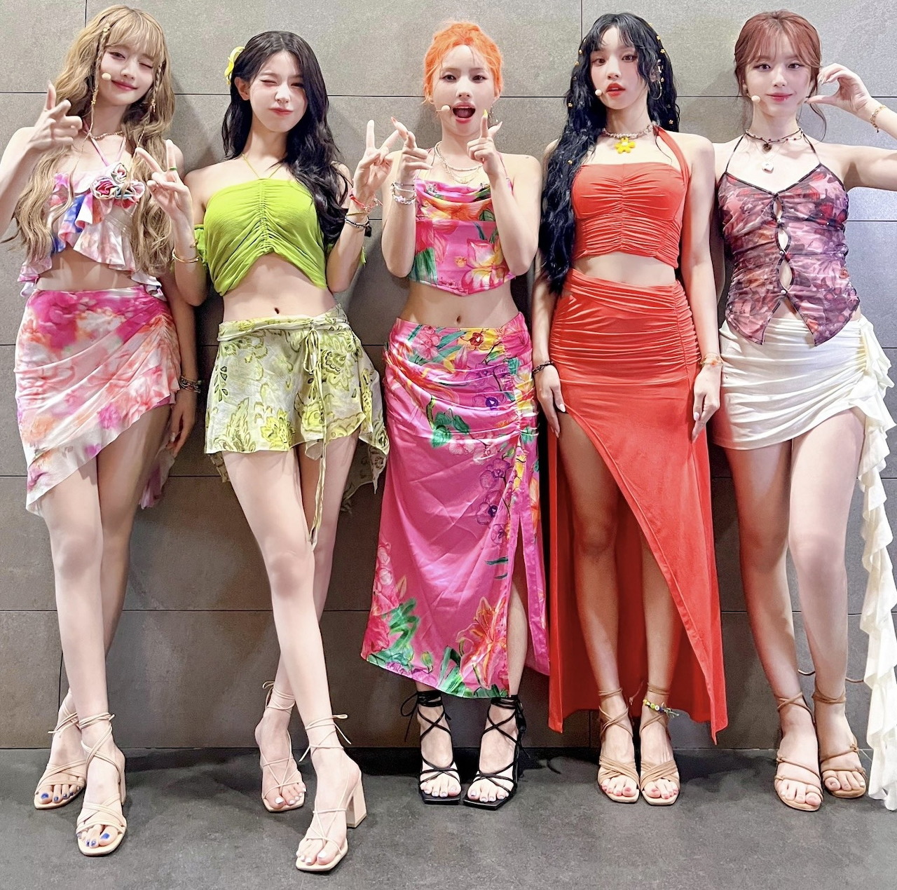 Five women standing in a row wearing colorful dresses and outfits in various styles