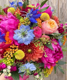 Dense bouquet of vibrant pink, blue, yellow, and orange flowers including roses, dahlias, and wildflowers
