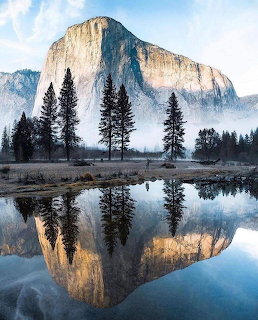 Granite mountain and pine trees reflected in a calm river