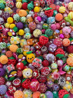 Densely packed colorful beads shaped like strawberries, fruits, and decorated with rhinestones and patterns