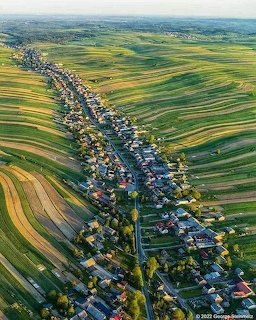Aerial view of Sułoszowa village lined along a road amid striped farmland fields in Poland.